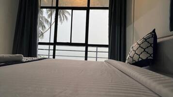 A hotel room with a large bed, a window with curtains, and a view of palm trees.