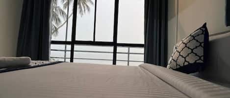 Una habitación de hotel con una cama grande, una ventana con cortinas y vistas a palmeras.