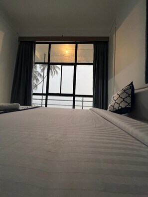 Una habitación de hotel con una cama grande, una ventana con cortinas y vistas a palmeras.