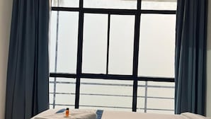 Habitación de hotel con cama, ventana con cortinas y vista al mar.