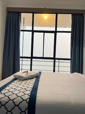 Habitación de hotel con cama, ventana con cortinas y vista al mar.