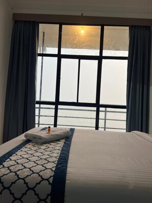 Una habitación de hotel con una cama, un ventanal con cortinas y vistas al mar.