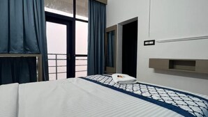 Habitación de hotel con una cama grande, una ventana con cortinas, una mesita de noche y un aplique de pared.