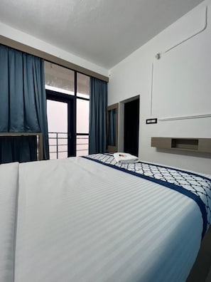 Habitación de hotel con una cama grande, una ventana con cortinas, una mesita de noche y un aplique de pared.