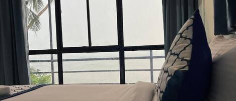 A hotel room with a large window, a bed with a pillow, and a view of palm trees.