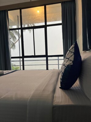 A hotel room with a large window, a bed with a pillow, and a view of palm trees.