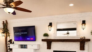 A living room with a fireplace, a flat-screen TV, and a ceiling fan.