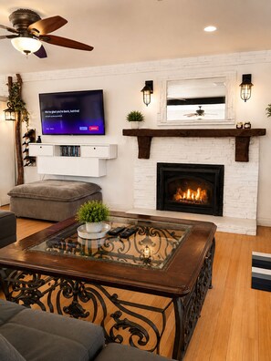 A living room with a fireplace, a flat-screen TV, and a ceiling fan.