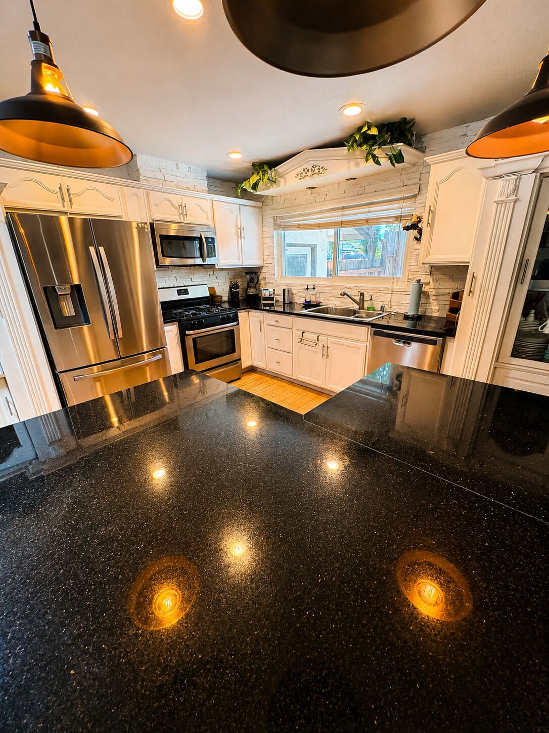 Una cocina moderna con electrodomésticos de acero inoxidable, encimera de granito negro e iluminación colgante.