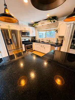 A modern kitchen with stainless steel appliances, a black granite countertop, and pendant lighting.
