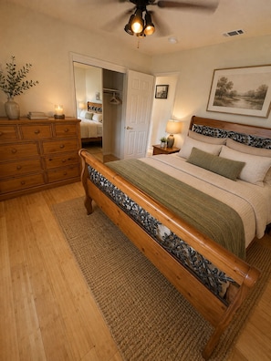 A bedroom with a wooden bed, a dresser, a mirror, a ceiling fan, and a framed picture on the wall.