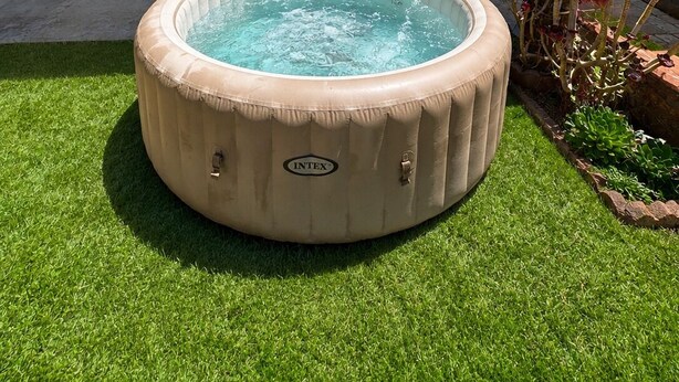 A hot tub in a backyard with a house in the background.