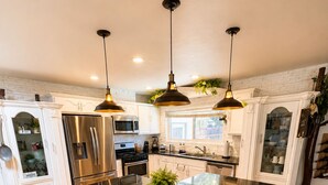 A modern kitchen with a central island, black bar stools, and pendant lighting.
