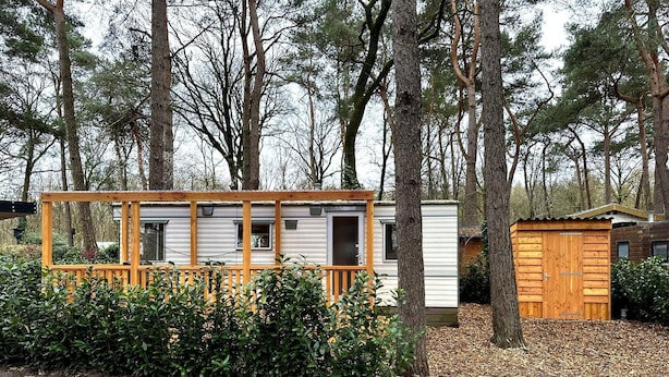 Ein Wohnmobil mit einer Holzterrasse, umgeben von dichtem Grün und Bäumen.