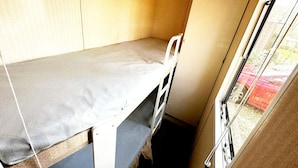 Ein kleiner, schmales Zimmer mit einem Bett, einem Fenster und einer Tür.