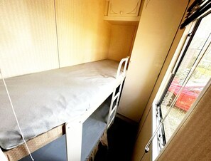 Um quarto pequeno e estreito com uma cama de solteiro, uma janela e uma porta.
