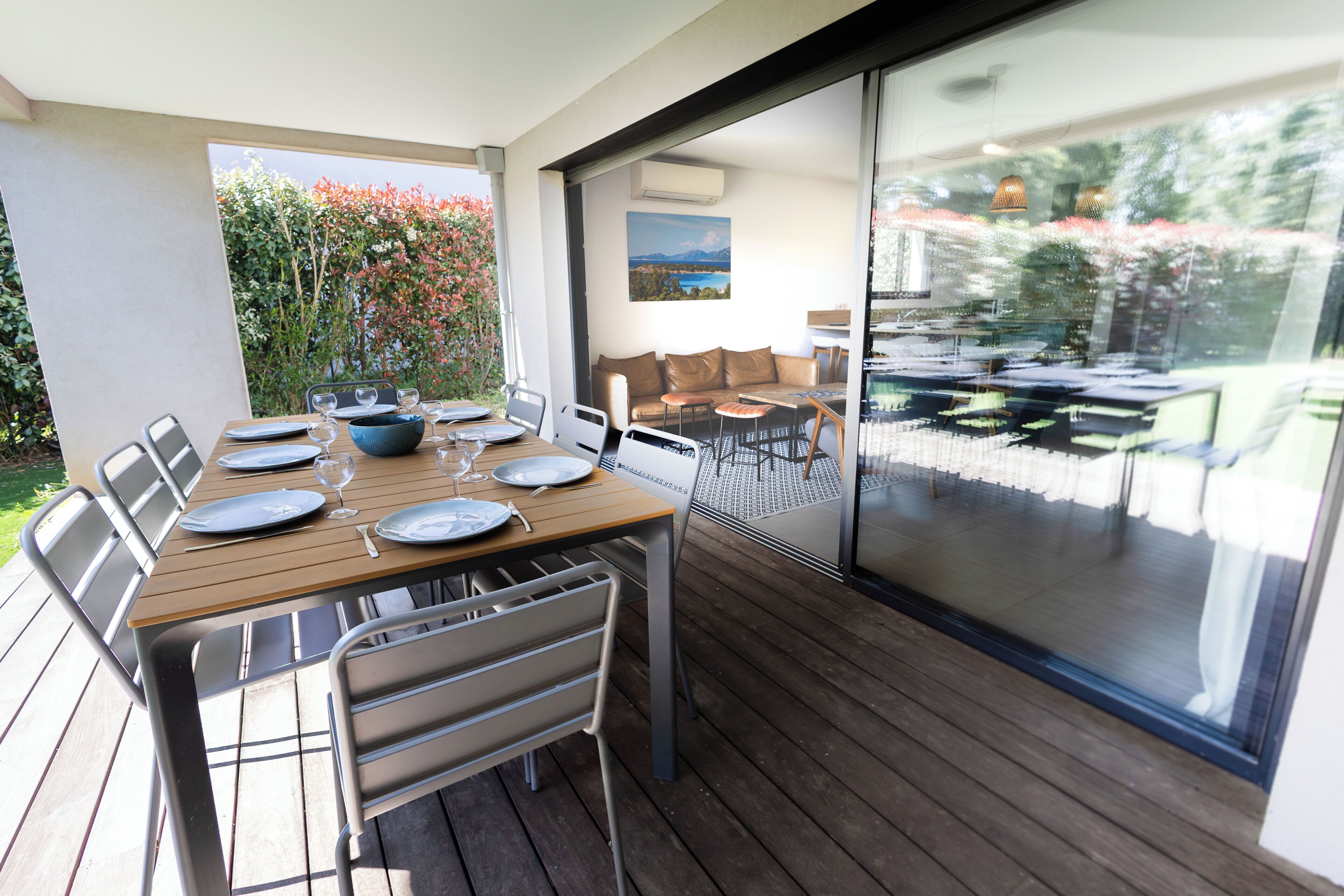A dining area with a wooden table set for four, metal chairs, and a view through a glass door to an outdoor space with a sofa and a table.