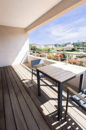 Eine Holzterrasse mit Tisch und Stuhl, mit Blick auf einen angelegten Garten mit verschiedenen Pflanzen und eine entfernte Ansicht von Häusern.