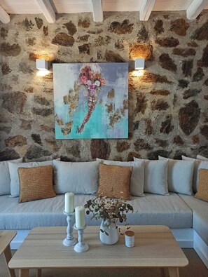 Ein Zimmer mit Steinwand, einer Couch mit Kissen, einem Tisch mit Kerzen und einer Vase sowie einem Gemälde.