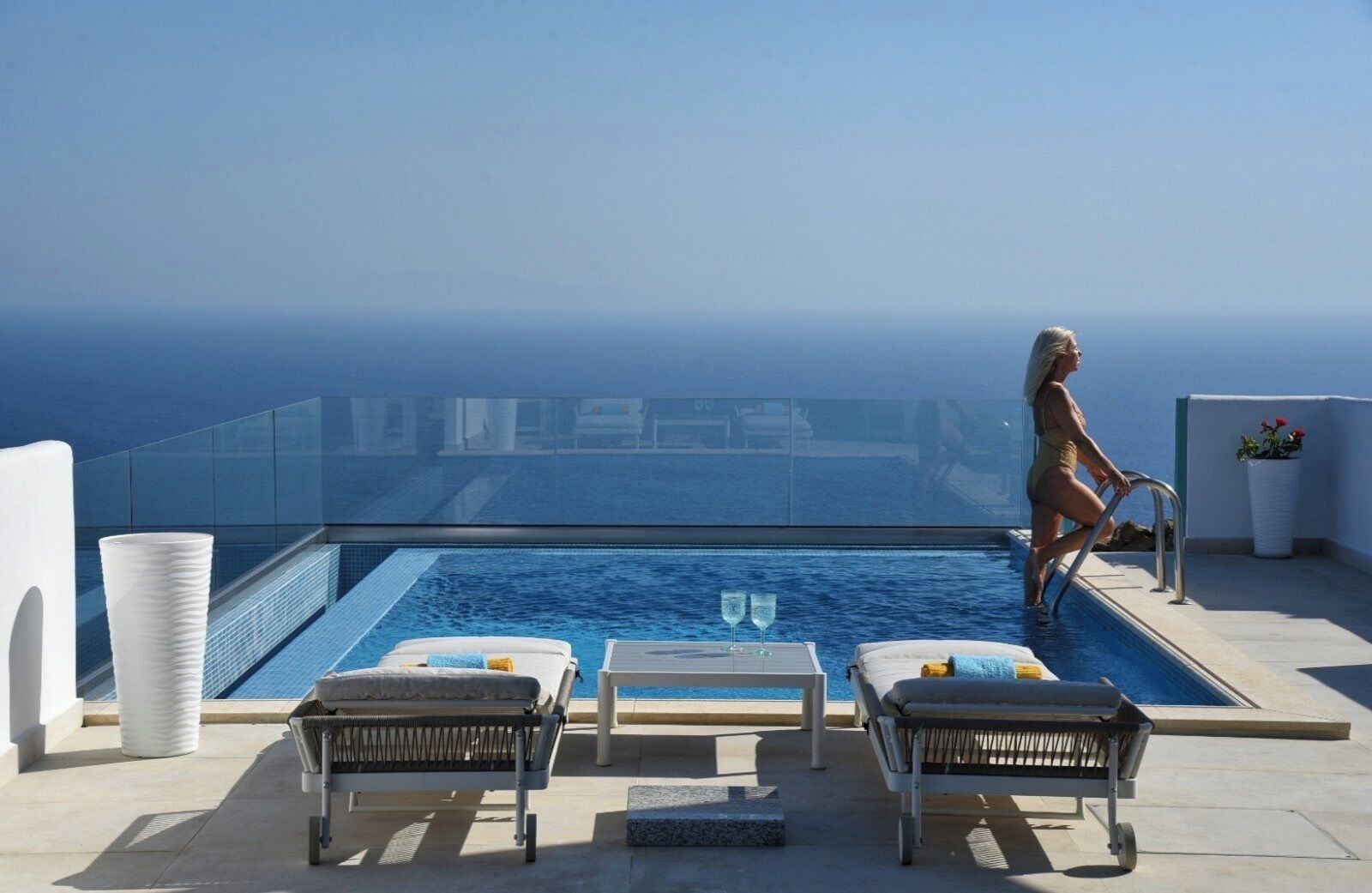A poolside area with lounge chairs, a glass balustrade, and a clear view of the sea.