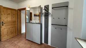Ein Zimmer mit Holztür, einer weißen Wand mit Spiegel, einem grauen Kleiderschrank und einem grauen Schrank mit Handtuchhalter.