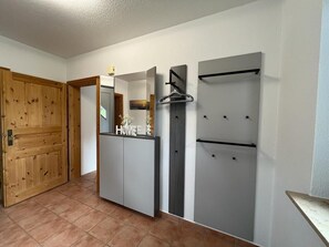 Ein Zimmer mit Holztür, einer weißen Wand mit Spiegel, einem grauen Kleiderschrank und einem grauen Schrank mit Handtuchhalter.
