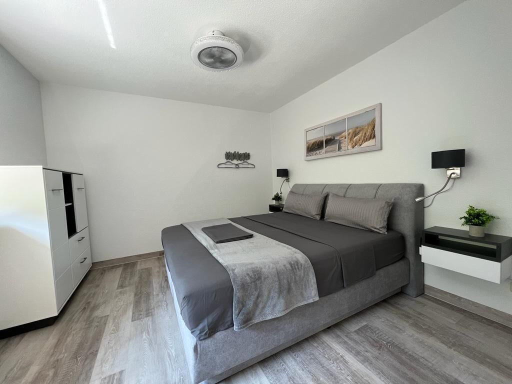 A modern bedroom with a bed, bedside tables, a wall-mounted TV, and a ceiling fan.