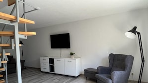 Ein modernes Wohnzimmer mit grauem Sofa, einem weißen Schrank, einem Flachbildfernseher und einer Stehlampe.