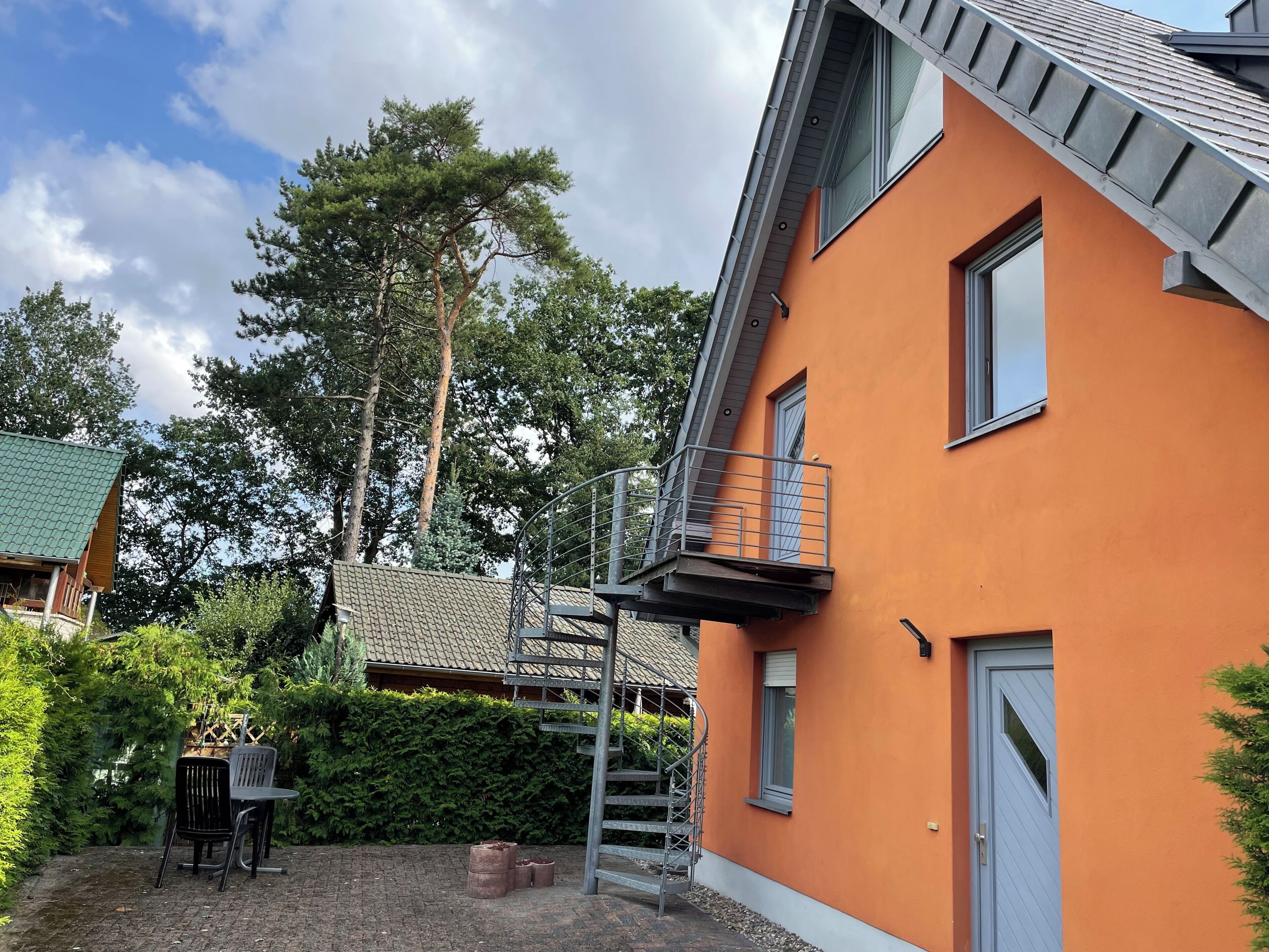 Uma casa moderna com telhado inclinado, varanda e pátio de tijolos com móveis de exterior.