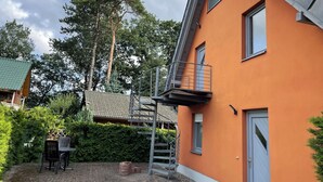 Ein modernes Haus mit Satteldach, einem Balkon und einer Ziegelterrasse mit Gartenmöbeln.