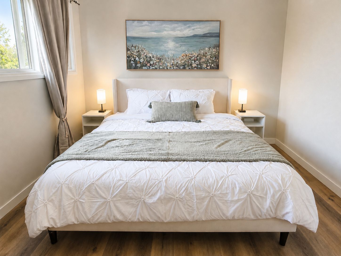 Quarto com uma cama grande, duas luminárias de cabeceira, um quadro sobre a cama e uma janela com cortinas.