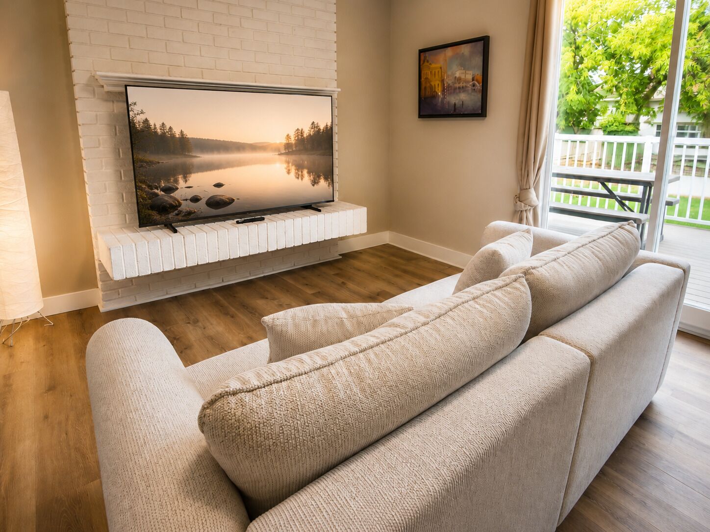 Ein Wohnzimmer mit Fernseher an einer weißen Ziegelwand, einem beigen Sofa und Holzboden.