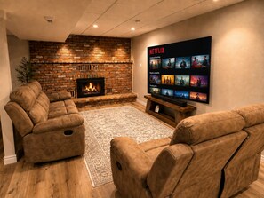 Ein gemütliches Wohnzimmer mit Kamin aus Backstein, bequemen Ledersofas und einem großen Flachbildfernseher, der Inhalte von Netflix zeigt.