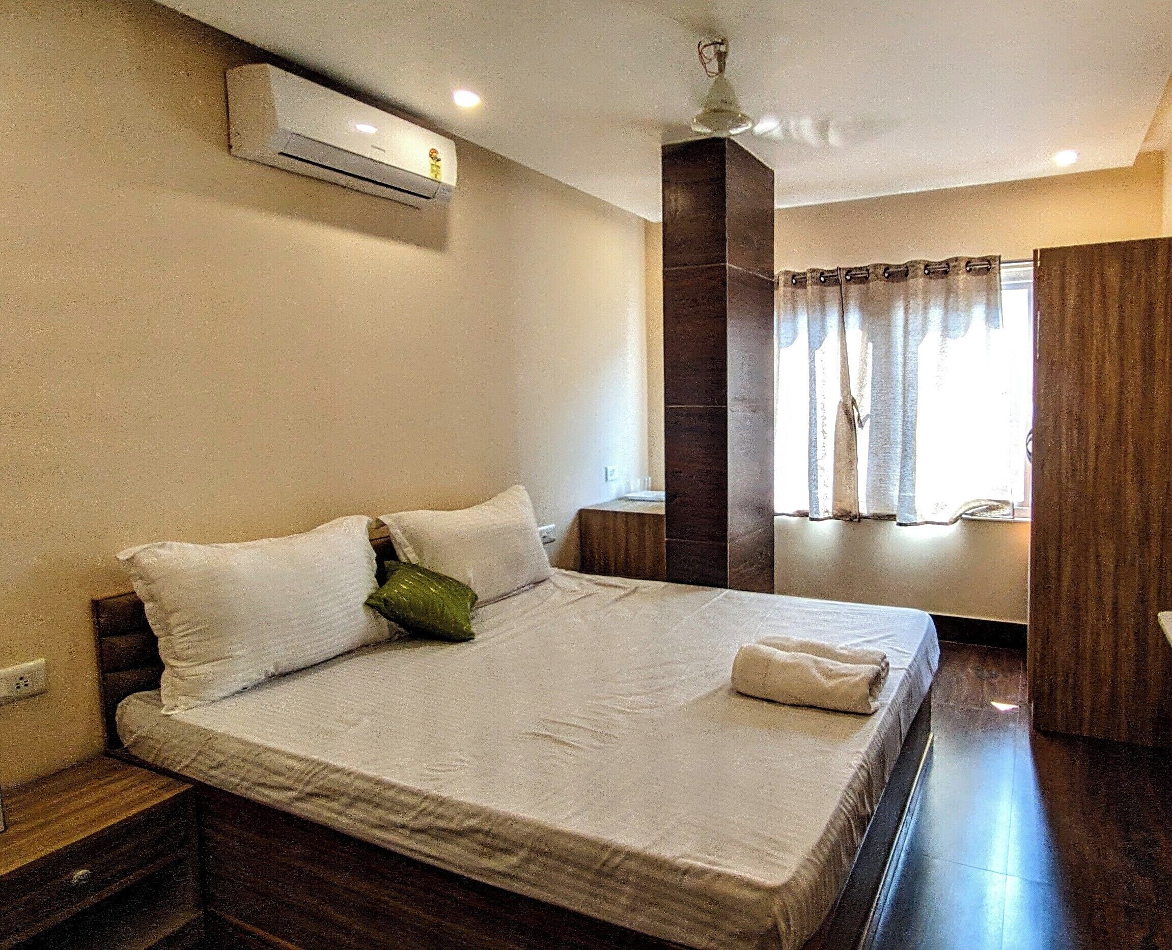 Una camera d'albergo con un letto, un comodino, una finestra con tende e un condizionatore d'aria.