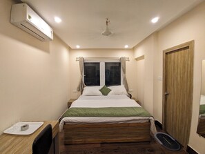 A bedroom with a bed, bedside table, window with curtains, and a door. - Hotel Vaikunth (Sahibganj)