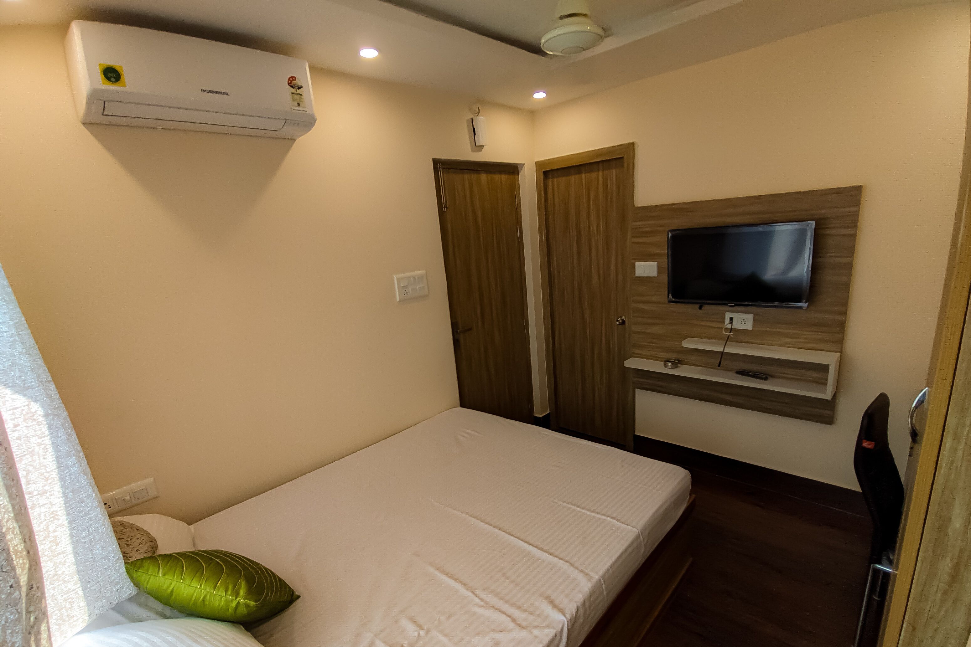 A bedroom with a bed, a TV mounted on the wall, and an air conditioner on the ceiling.
