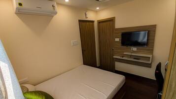 A bedroom with a bed, a TV mounted on the wall, and an air conditioner on the ceiling.