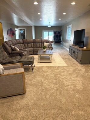 A living room with a sectional sofa, a coffee table, a TV on a cabinet, and a ceiling fan. - Spacious 7-bedroom house in beautiful North Salt Lake (North Salt Lake)