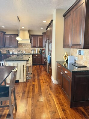A kitchen with dark wooden cabinets, a central island, and a dining area with a table and chairs. - Spacious 7-bedroom house in beautiful North Salt Lake (North Salt Lake)