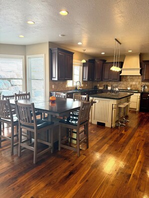 A spacious kitchen with wooden flooring, dark cabinets, a central island with stools, and pendant lighting. - Spacious 7-bedroom house in beautiful North Salt Lake (North Salt Lake)