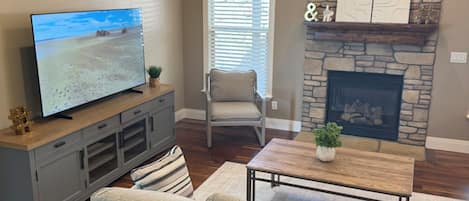 Una sala de estar con televisor, chimenea de piedra, sofá y mesa de comedor.