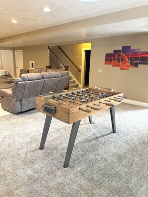 A room with a foosball table, a gray sofa, and a staircase. - Spacious 7-bedroom house in beautiful North Salt Lake (North Salt Lake)