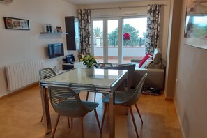 A dining area with a glass table, four chairs, a TV, a potted plant, and a sofa. - Belvilla by OYO Dolce Vita (Orihuela Costa)