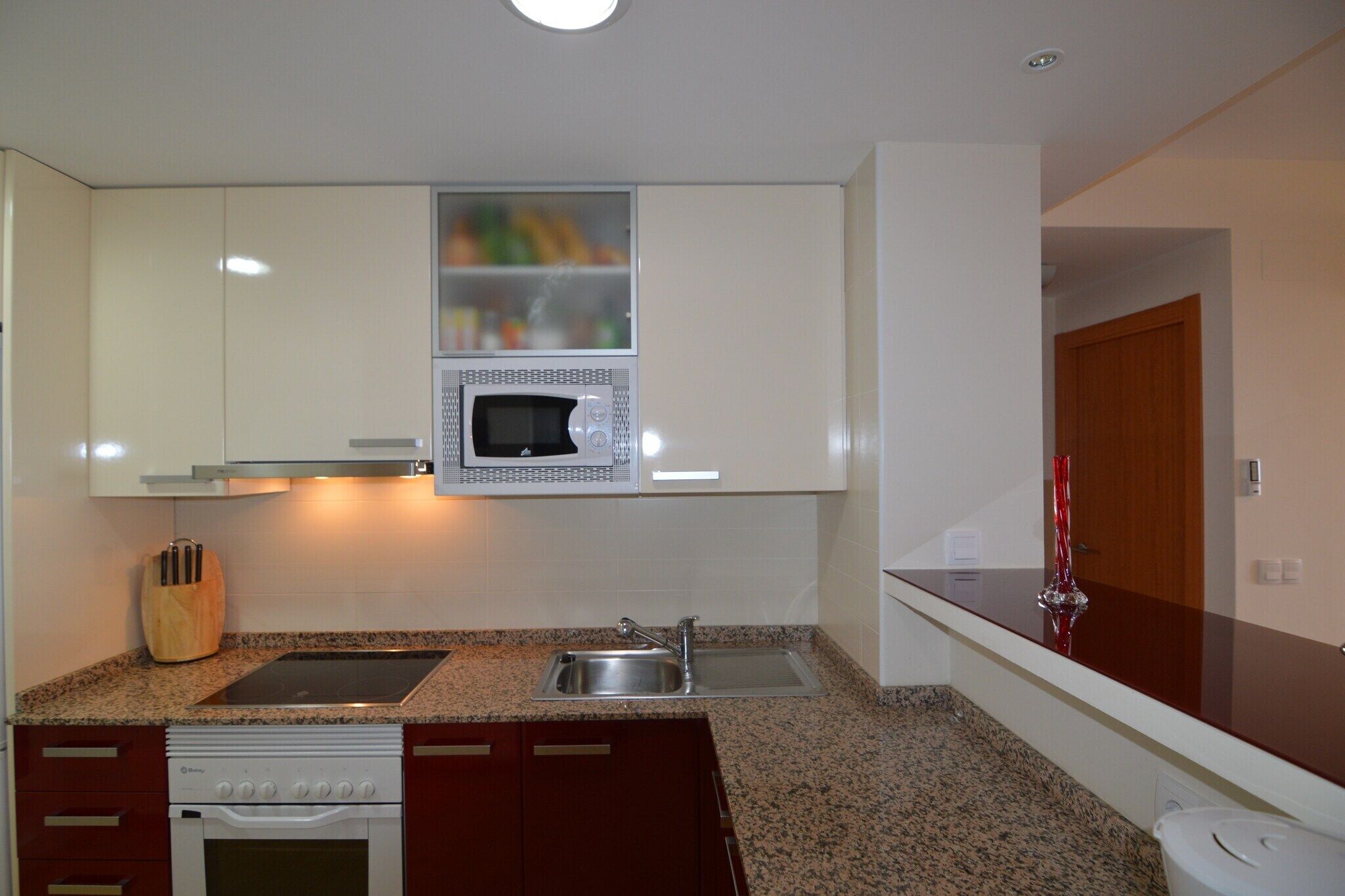A modern kitchen with white cabinets, a built-in microwave, granite countertops, a stainless steel sink, and a dishwasher. - Belvilla by OYO Dolce Vita (Orihuela Costa)