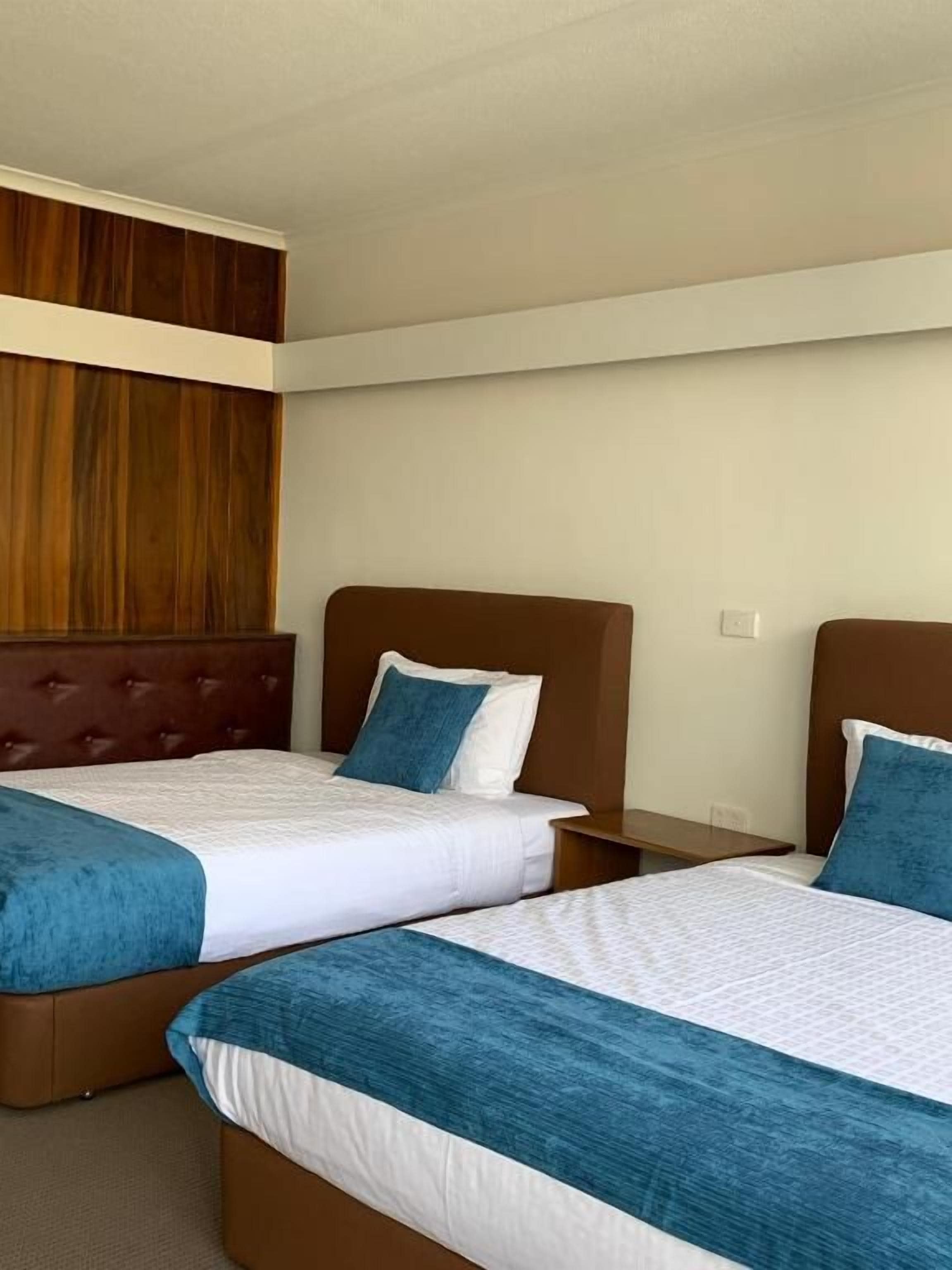 A hotel room with two beds, each with a headboard and a pillow.