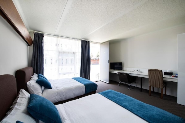 A hotel room with two beds, a desk, a chair, and a television.