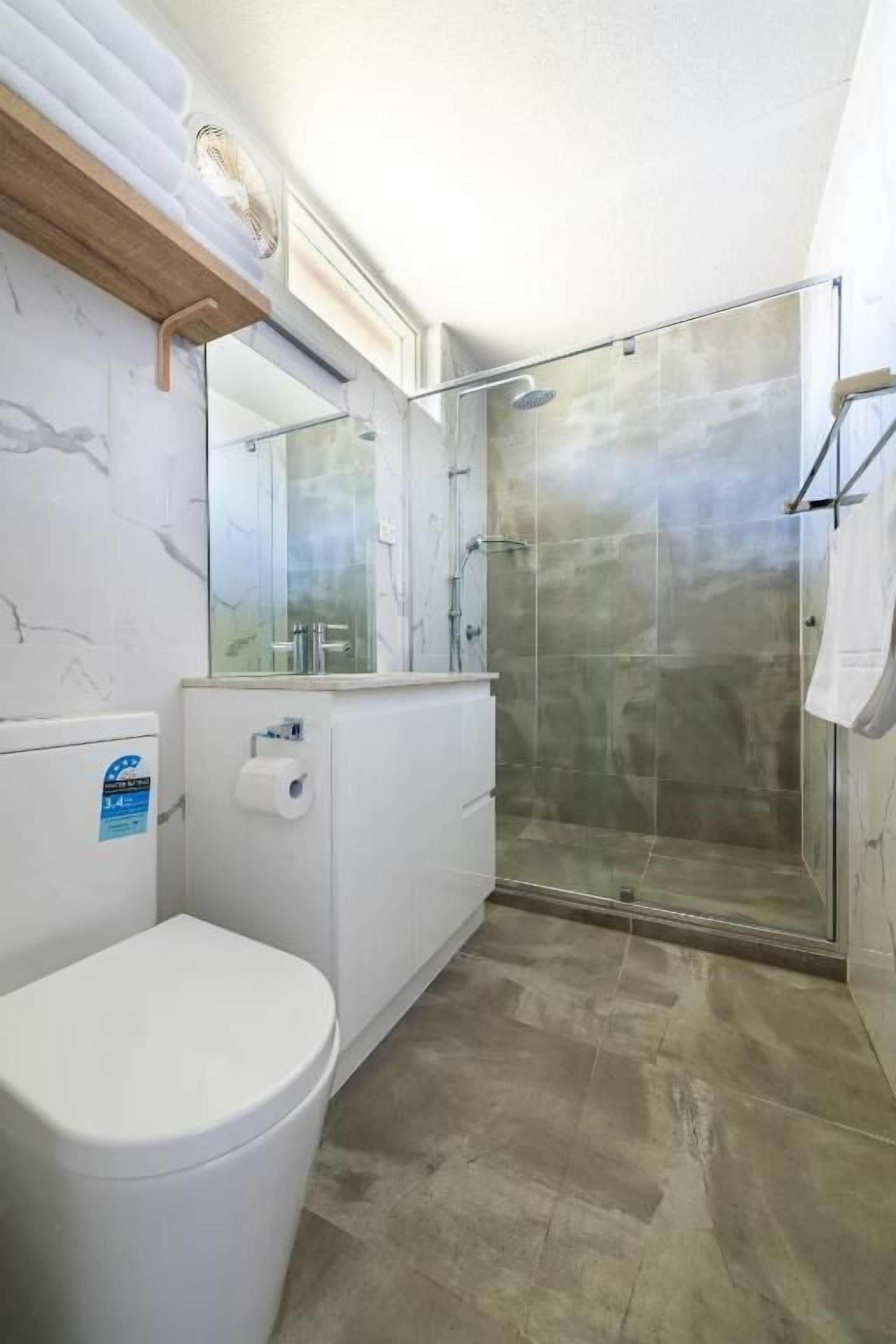 A bathroom with a toilet, a shower enclosure, and a mirror.