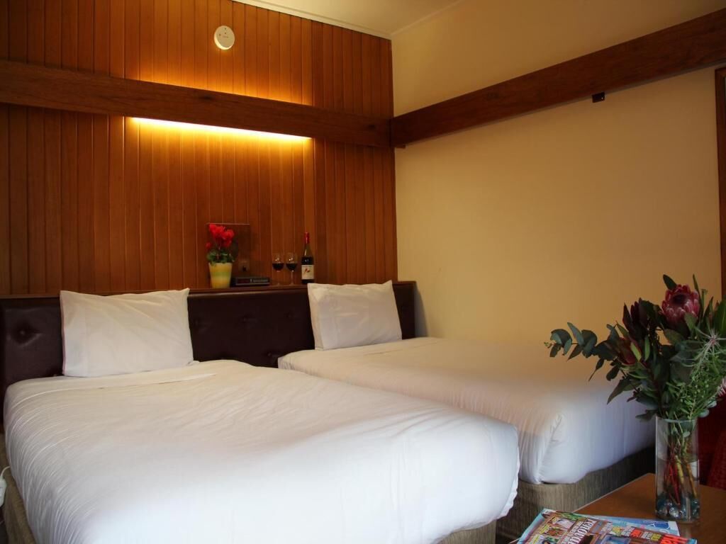 A hotel room with two beds, a wooden headboard, a nightstand with a vase of flowers, and a magazine on the table.