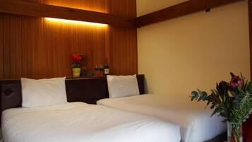 A hotel room with two beds, a wooden headboard, a nightstand with a vase of flowers, and a magazine on the table.