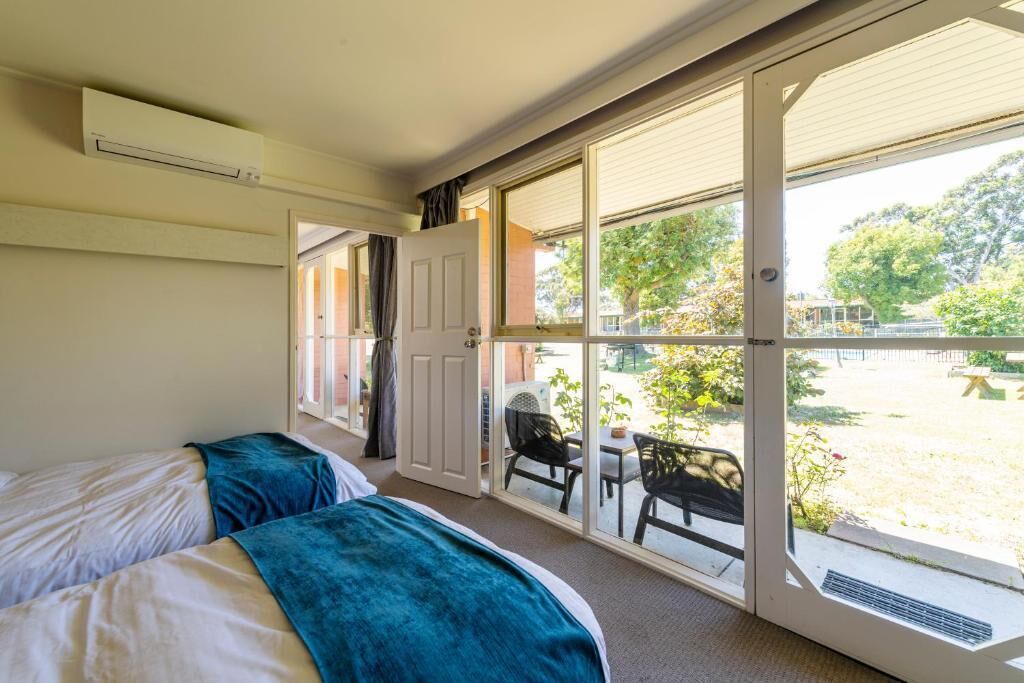 Una habitación con dos camas y un ventanal corredero que da a un espacio exterior con una mesa y sillas.